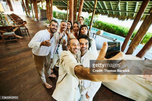 wide shot of gay couple taking a selfie with friends during wedding reception at luxury tropical villa - logement social stockfoto's en -beelden