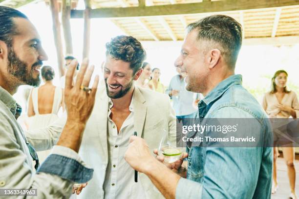 medium shot of groom laughing with friends at wedding reception at luxury tropical villa - party guest stock pictures, royalty-free photos & images