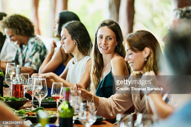 medium wide shot of smiling woman dining with friends during wedding reception dinner at luxury tropical villa - wedding guests stockfoto's en -beelden