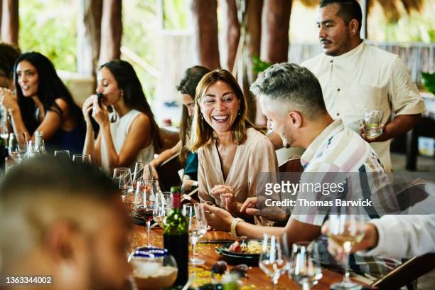 medium wide shot of woman laughing with friend during wedding reception dinner at luxury tropical resort - medium group of people foto e immagini stock
