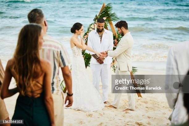 wide shot of bride covering mouth in surprise during wedding on tropical beach in front of friends and family - front on groom and bride stock pictures, royalty-free photos & images