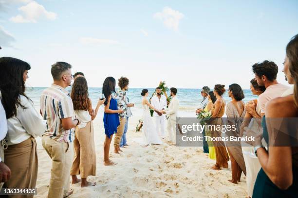 extreme wide shot of bride and groom getting married on tropical beach in front of friends and family - destination wedding imagens e fotografias de stock