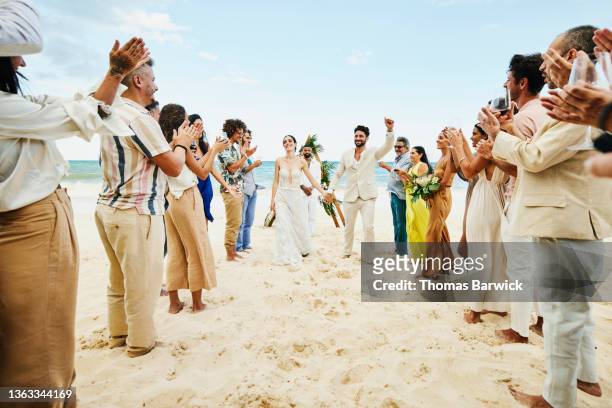 wide shot of bride and groom walking down aisle after wedding ceremony on tropical beach while friends and family celebrate - destination wedding imagens e fotografias de stock