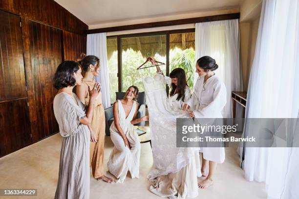 wide shot of smiling bride admiring wedding dress with bridesmaids in luxury hotel room before getting dressed for wedding - europe bride bildbanksfoton och bilder