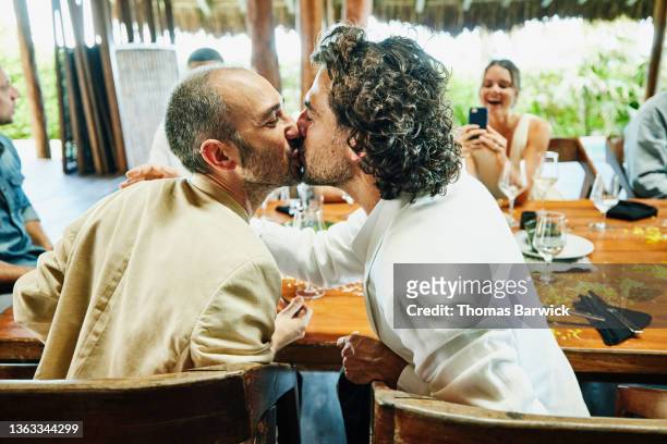 medium wide shot of gay couple kissing during wedding reception dinner at luxury tropical resort - dinner jacket stock-fotos und bilder