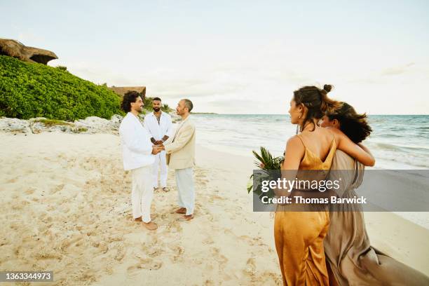 wide shot of smiling gay couple getting married in front of friends and family at tropical beach resort - destination wedding imagens e fotografias de stock
