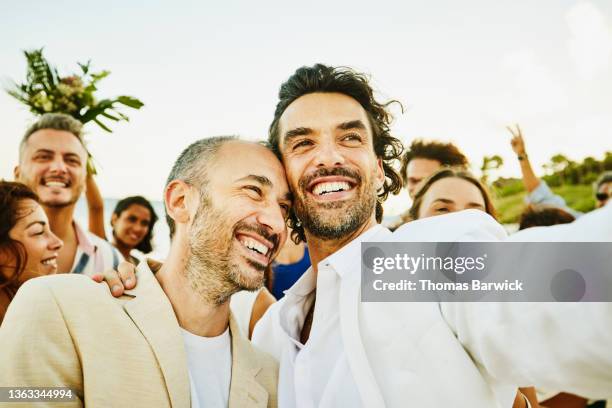 medium shot of smiling gay couple taking selfie with friends and family after wedding ceremony on tropical beach - gay marriage stockfoto's en -beelden