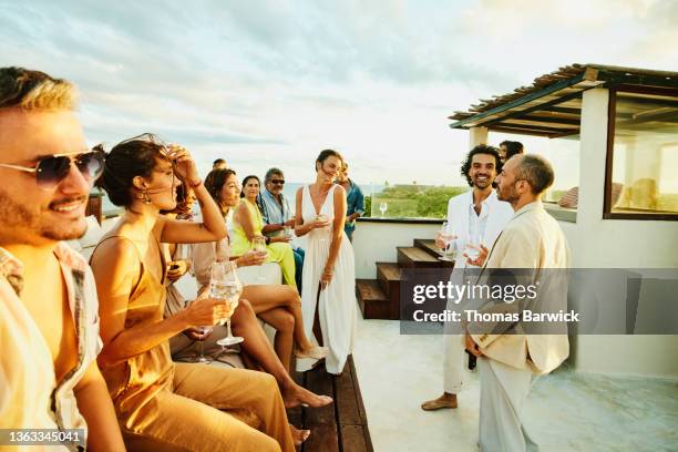 wide shot of smiling friends and family celebrating on rooftop deck after wedding at tropical resort - soirée chic stock pictures, royalty-free photos & images