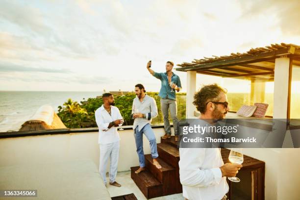 medium wide shot of friends hanging out on rooftop deck after wedding at tropical resort - medium group of people foto e immagini stock