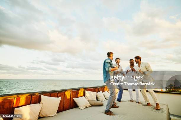 Wide shot of male friends dancing on rooftop deck after wedding at tropical resort