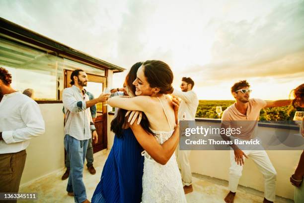 medium wide shot of smiling bride hugging friend during party on rooftop deck after wedding at tropical resort - wedding after party fotografías e imágenes de stock