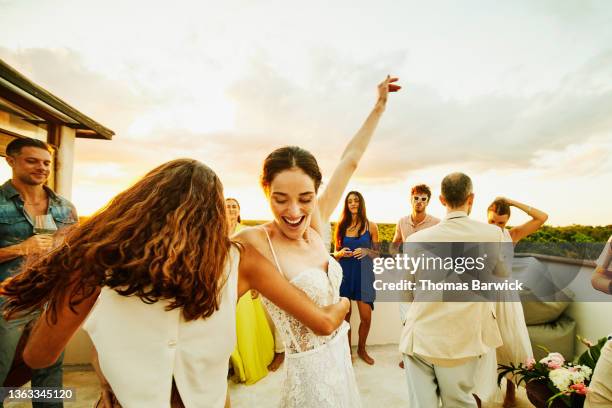 medium wide shot of smiling bride and friend dancing during party on rooftop deck after wedding at tropical resort - ダンス ストックフォトと画像