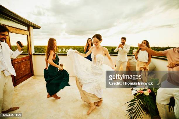 wide shot of bride dancing with friends during sunset rooftop party after wedding at tropical resort - wedding after party stock pictures, royalty-free photos & images