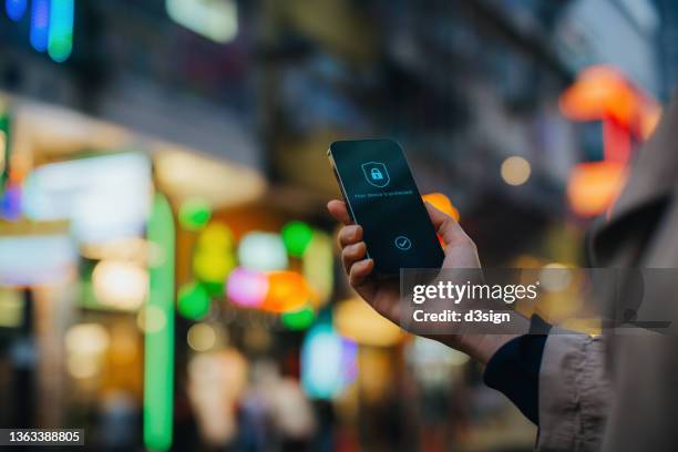 close up of woman's hand using smartphone in downtown city street against multi-coloured and illuminated urban city scene, with a security key lock icon on the smartphone screen. privacy protection, internet and mobile security concept - privat skylt bildbanksfoton och bilder