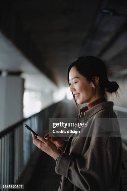 beautiful smiling young asian woman checking her smartphone for new messages from friends while walking on urban bridge in the city. staying socially connected anytime anywhere - leading people across a bridge stock pictures, royalty-free photos & images