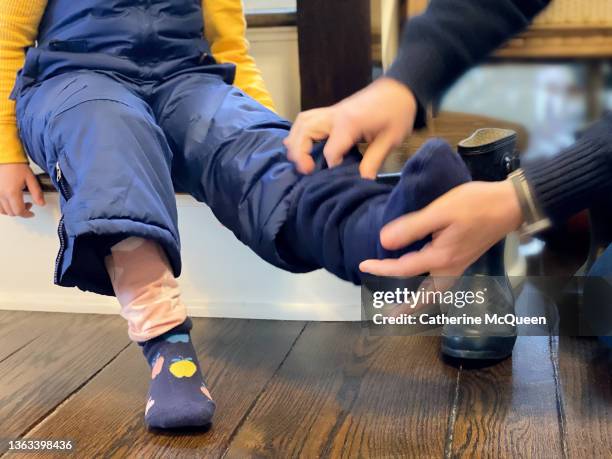 dad helps young mixed-race daughter wearing snow pants to put on rubber boots & boot liner socks - wellington boot stockfoto's en -beelden
