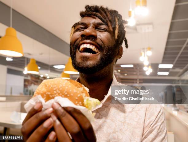 young man enjoying having burger at a restaurant - eating burger bildbanksfoton och bilder