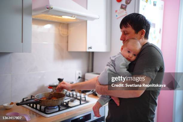 father in the kitchen with a baby in his arms - gas stove cooking stock pictures, royalty-free photos & images