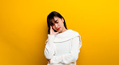 Drowsiness. A beautiful woman wearing a white sweater. Tired, yawning, tired, hands covering his mouth, eyes closed and sleepy on a yellow background