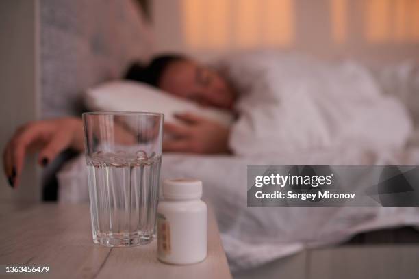 pills and glass water on bedside table near woman - pijnstiller stockfoto's en -beelden
