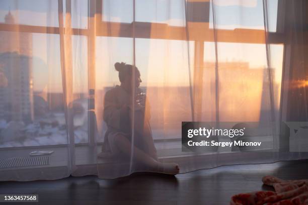 woman with water resting near window at sunset - partiell lichtdurchlässig stock-fotos und bilder
