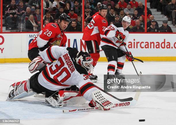 Zenon Konopka of the Ottawa Senators skates to the net looking for a rebound as Martin Brodeur of the New Jersey Devils makes a save with Chris Neil...