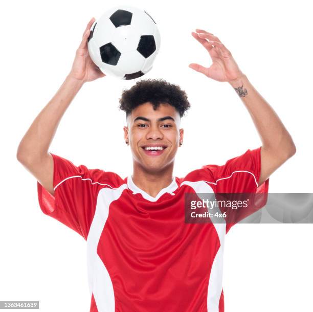 generation z young male athlete standing in front of white background wearing soccer uniform and holding soccer ball and playing soccer - sport and using sports ball - soccer jerseys stock pictures, royalty-free photos & images