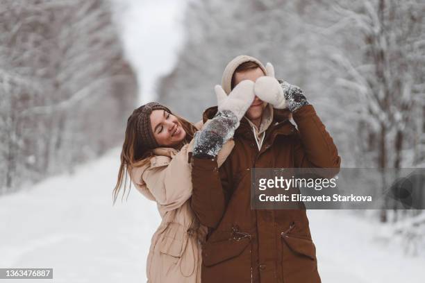 a happy couple in love in warm clothes are walking, having fun and hugging celebrating the valentine's day holiday among the trees in a snowy forest outdoors. a young man and a woman spend time together on a date on a trip outside the city - russia travel stock pictures, royalty-free photos & images