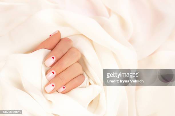 smooth elegant silk or satin and woman's hand with pastel color manicure and red hearts. - fingernagel stock-fotos und bilder