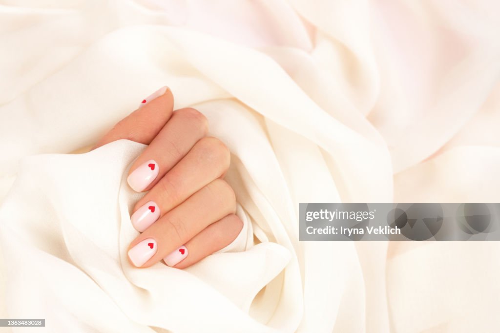 Smooth elegant silk or satin and woman's hand with pastel color manicure and red hearts.