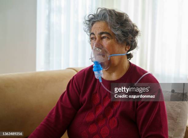 donna anziana che fa inalazione attraverso maschera di ossigeno a casa - maschera per l'ossigeno foto e immagini stock