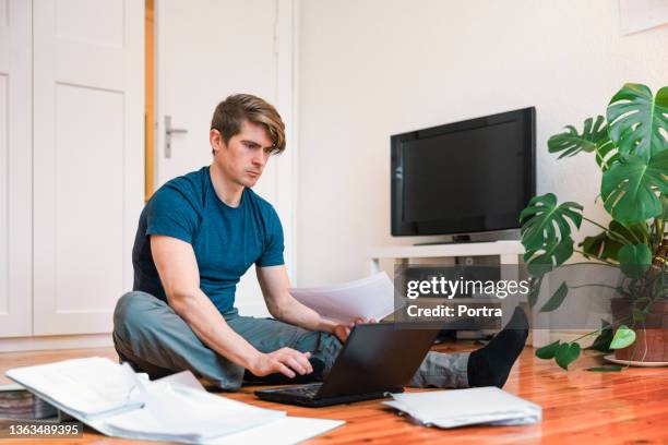 ラップトップを使用して家計費を支払うために床に座っている男 - bank statement ストックフォトと画像
