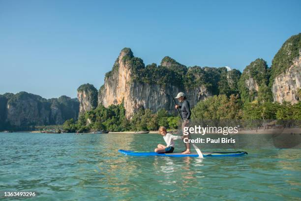 mother and son playing on sup paddleboard, railay beach, ao nang, krabi, thailand - mature paddleboard stock pictures, royalty-free photos & images