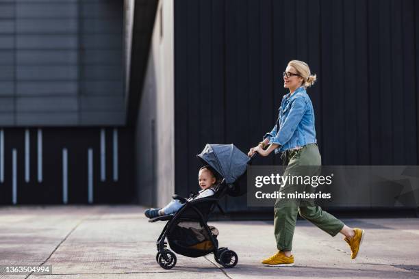 cheerful mother on a city walk pushing her daughter in a stroller - kinderwagen stockfoto's en -beelden
