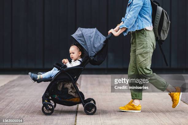 anonyme mutter auf einem stadtspaziergang schiebt ihre tochter in einem kinderwagen - baby stroller stock-fotos und bilder