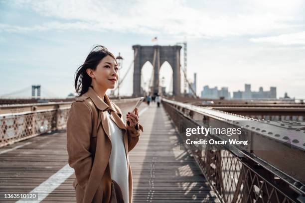 confident businesswoman using smart phone on brooklyn bridge, new york - age of extinction new york premiere stockfoto's en -beelden