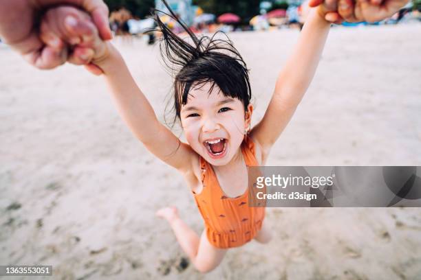 personal perspective of father holding little daughter's hand, swinging her around and having fun playing on the beach. outdoor summer fun, playtime with father - family summer holiday stock-fotos und bilder