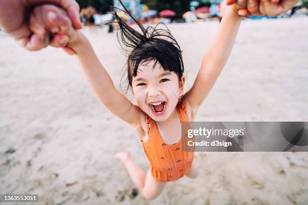 personal perspective of father holding little daughter's hand, swinging her around and having fun playing on the beach. outdoor summer fun, playtime with father - turn fotografías e imágenes de stock