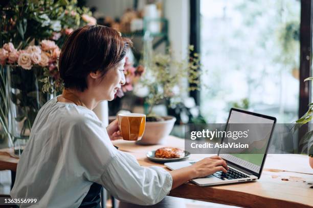 fleuriste asiatique souriante et confiante, propriétaire d’un magasin de fleurs pour petites entreprises, analysant les performances de l’entreprise sur ordinateur portable, signalant une croissance des revenus, se sentant heureux et satisfait. croiss - self employed photos et images de collection