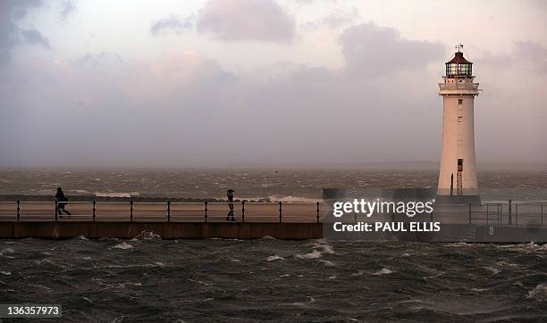 People walk towards Perch Rock lighthouse at the mouth of the River Mersey during a spell of high winds in New Brighton, north-west England on...