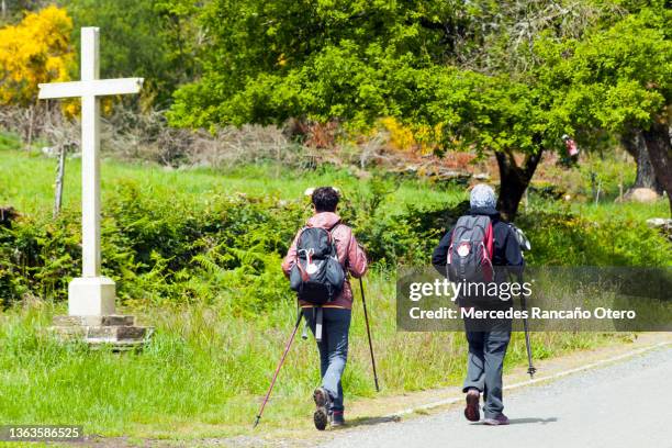 due donne pellegrine nel 'cammino di santiago' che camminano con una grande croce religiosa. - pellegrino foto e immagini stock