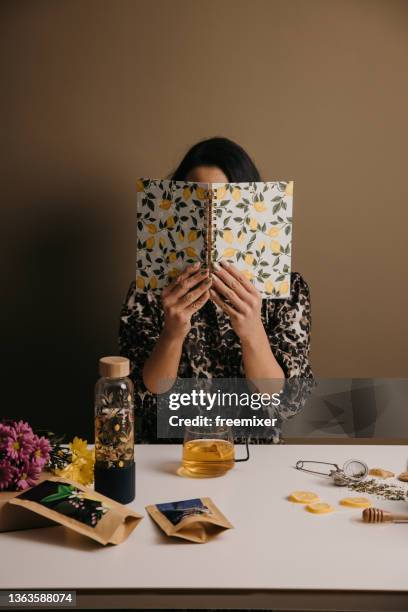 young woman hides behind a notebook above the table with healthy groceries - herbal tea bag stock pictures, royalty-free photos & images