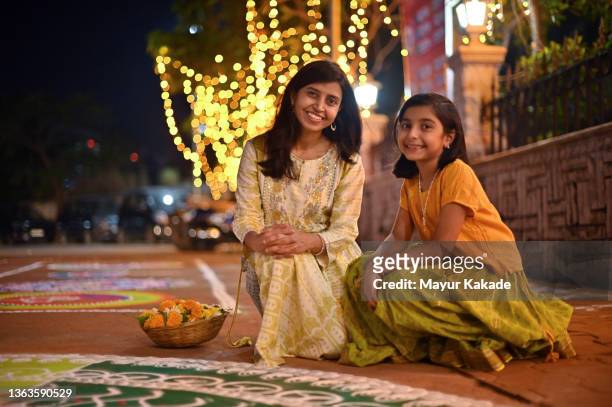mother and daughter sitting together near a rangoli design - diwali family stock-fotos und bilder