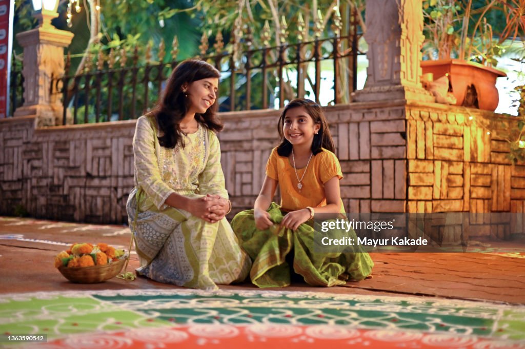 Mother and daughter sitting together near a Rangoli design