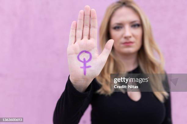 female with the feminist symbol painted in purple on her hand - droits de la femme photos et images de collection
