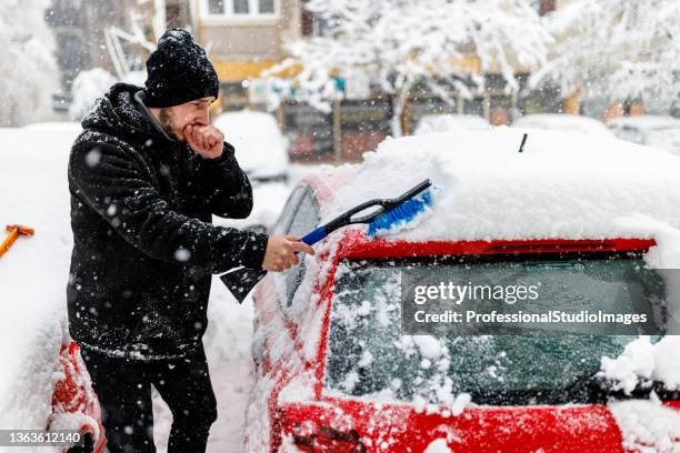 a young man is cleaning snow from a car with a brush. - 25 january stock pictures, royalty-free photos & images