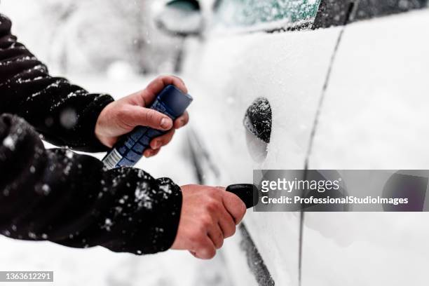 un homme a des problèmes de neige avec une voiture, alors il dégèle la porte. - serrure photos et images de collection
