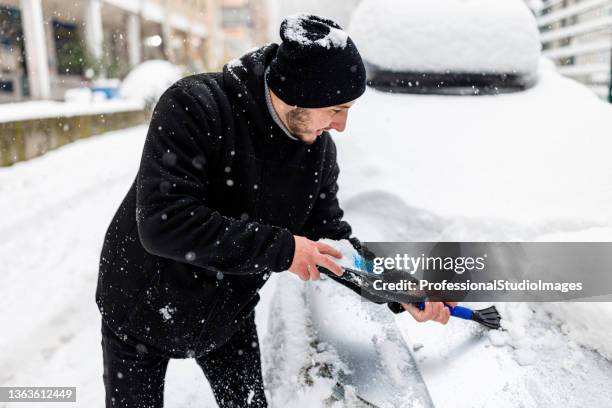 der mensch reinigt einen schnee aus einem auto mit einer bürste. - scraping stock-fotos und bilder