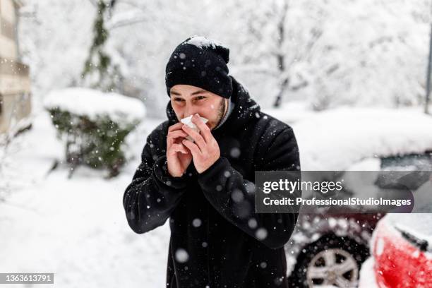 young man is blowing a nose during a winter day. - cold virus stock pictures, royalty-free photos & images