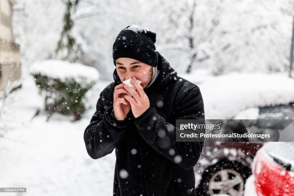 Young Man is Blowing a Nose During a Winter Day.